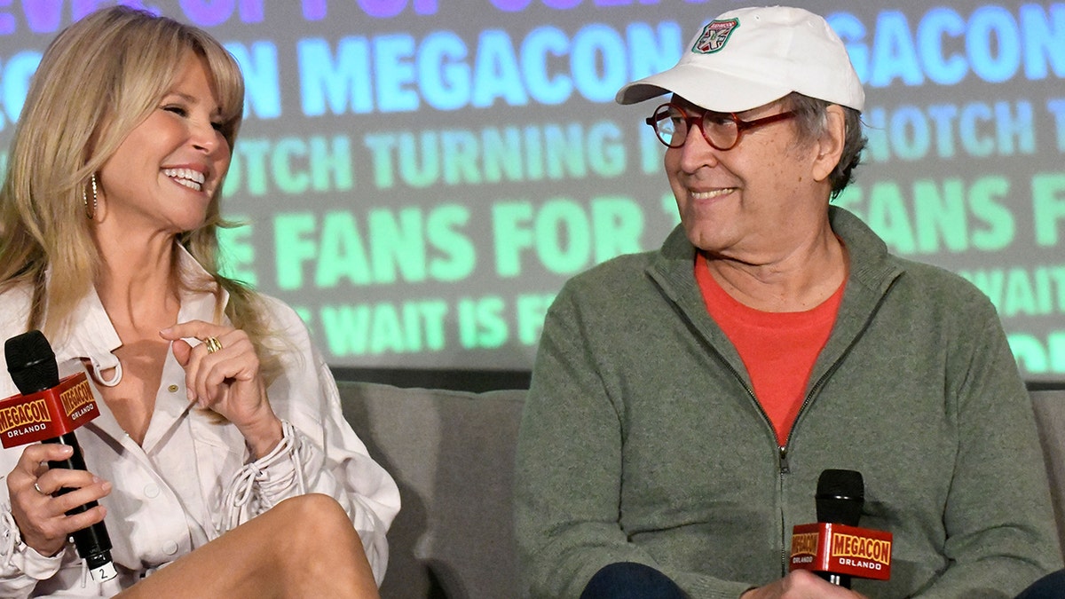 Christie Brinkley smiling and sitting next to Chevy Chase.