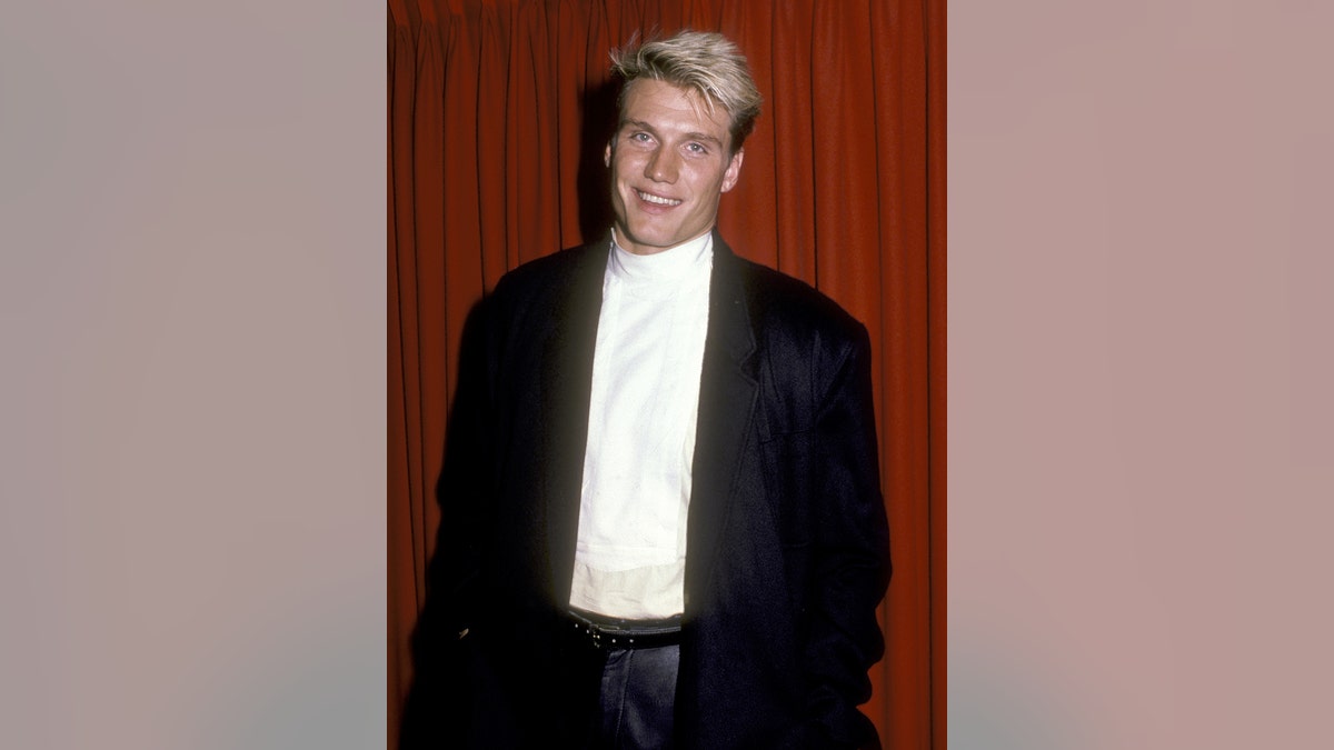 A young Dolph Lundgren wearing a black blazer and a white shirt.