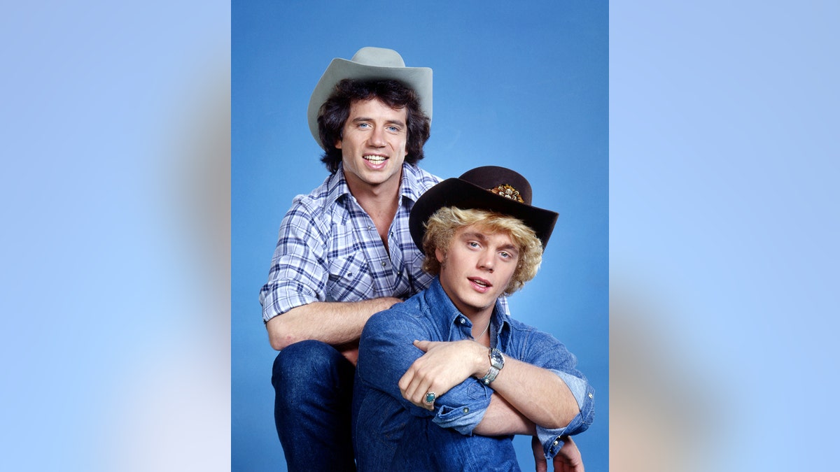 Tom Wopat and John Schneider posing in costume as Bo and Luke Duke.