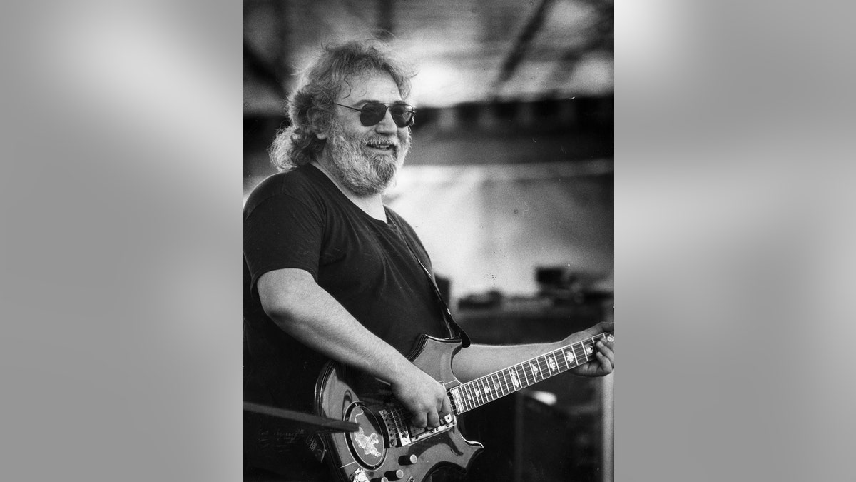 A black and white photo of Jerry Garcia smiling and playing guitar.