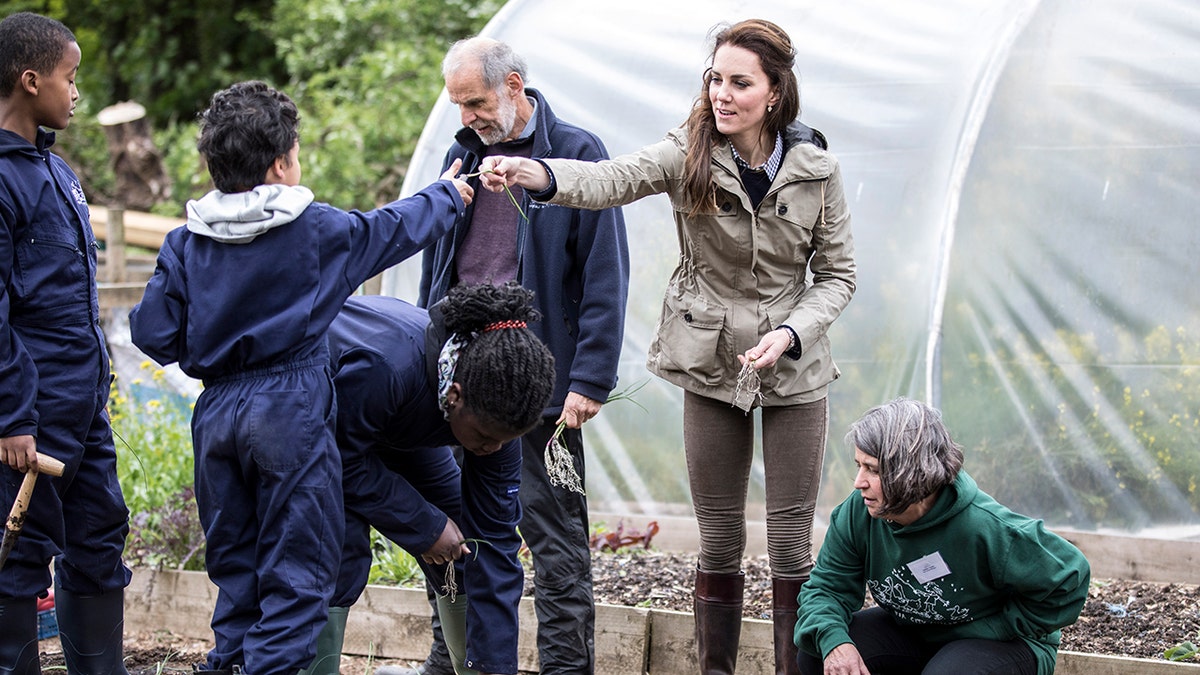 Kate Middleton handing out a plant to a child on a farm.