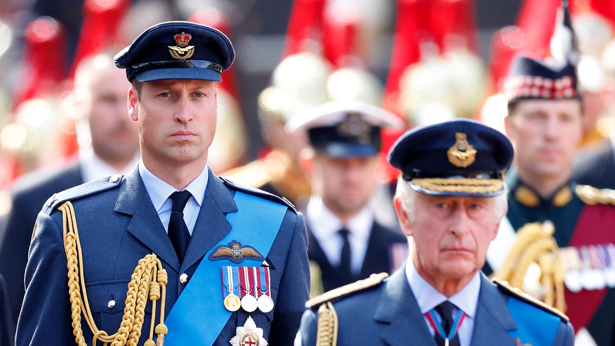 Prince William walking behind his father King Charles as they're both in uniform.