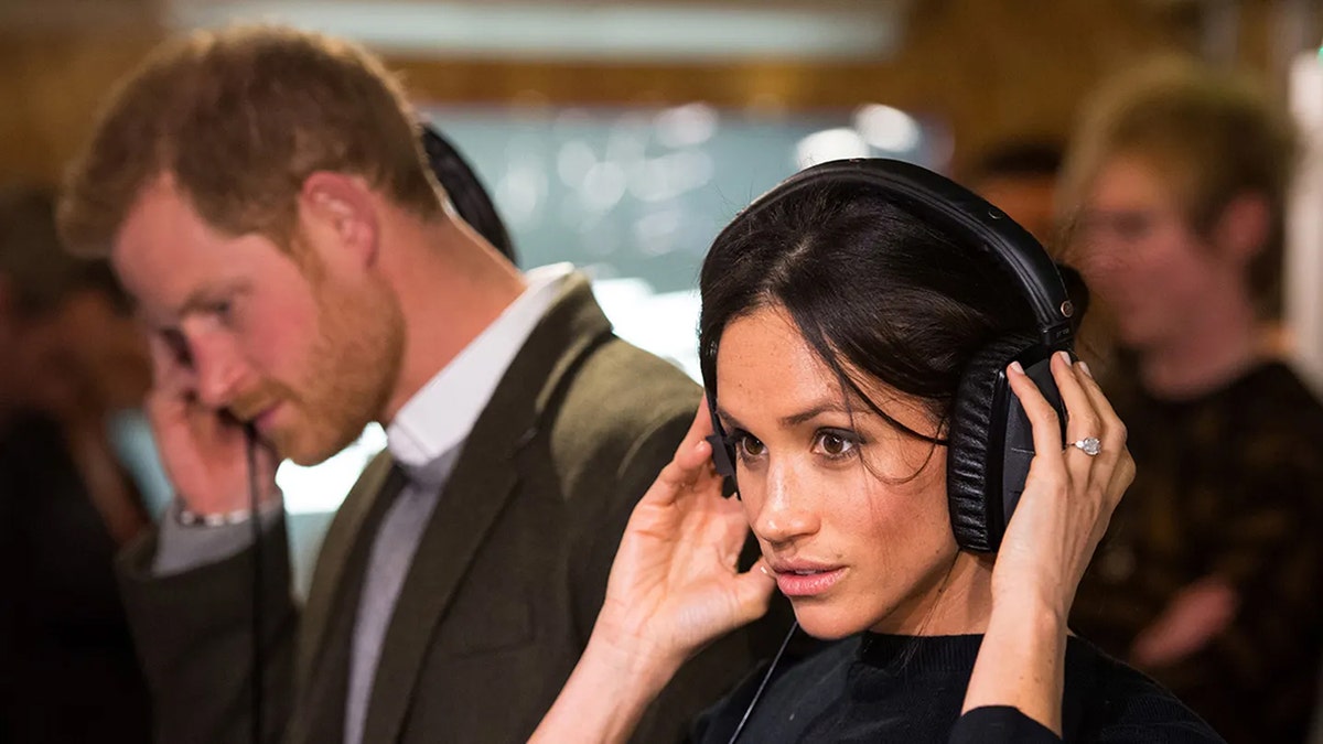 Prince Harry and Meghan Markle are listening to headphones.