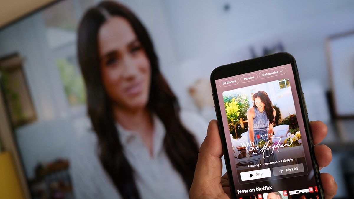 Certaines personnes ont des smartphones pour afficher le nouveau salon de Meghan Markle de Netflix. "Avec amour, Megan"devant un écran de télévision montrant des images de l'émission.