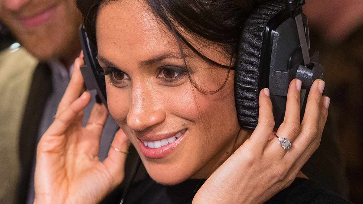A close-up of Meghan Markle smiling while listening to headphones.