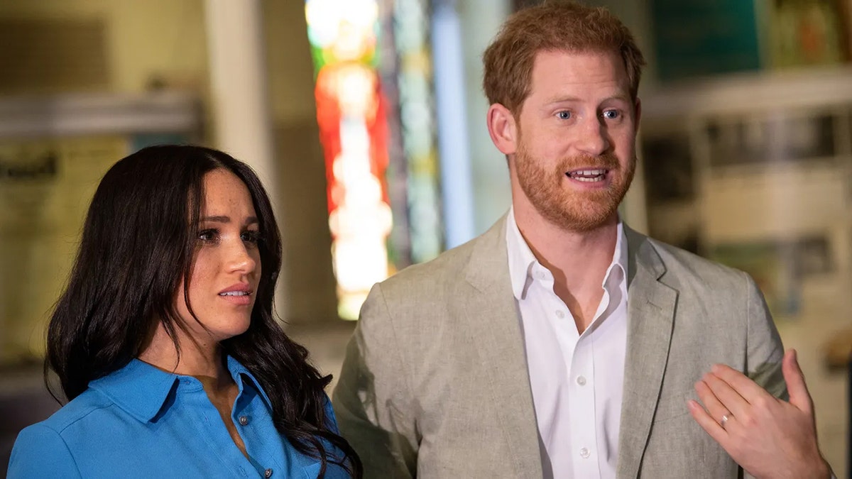Meghan Markle appears to be upset with Prince Harry in a beige suit and a blue shirt talking to him.