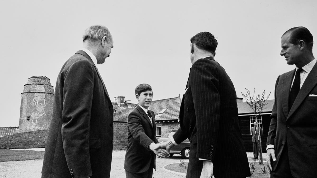 A young Prince Charles shaking hand with an older man.
