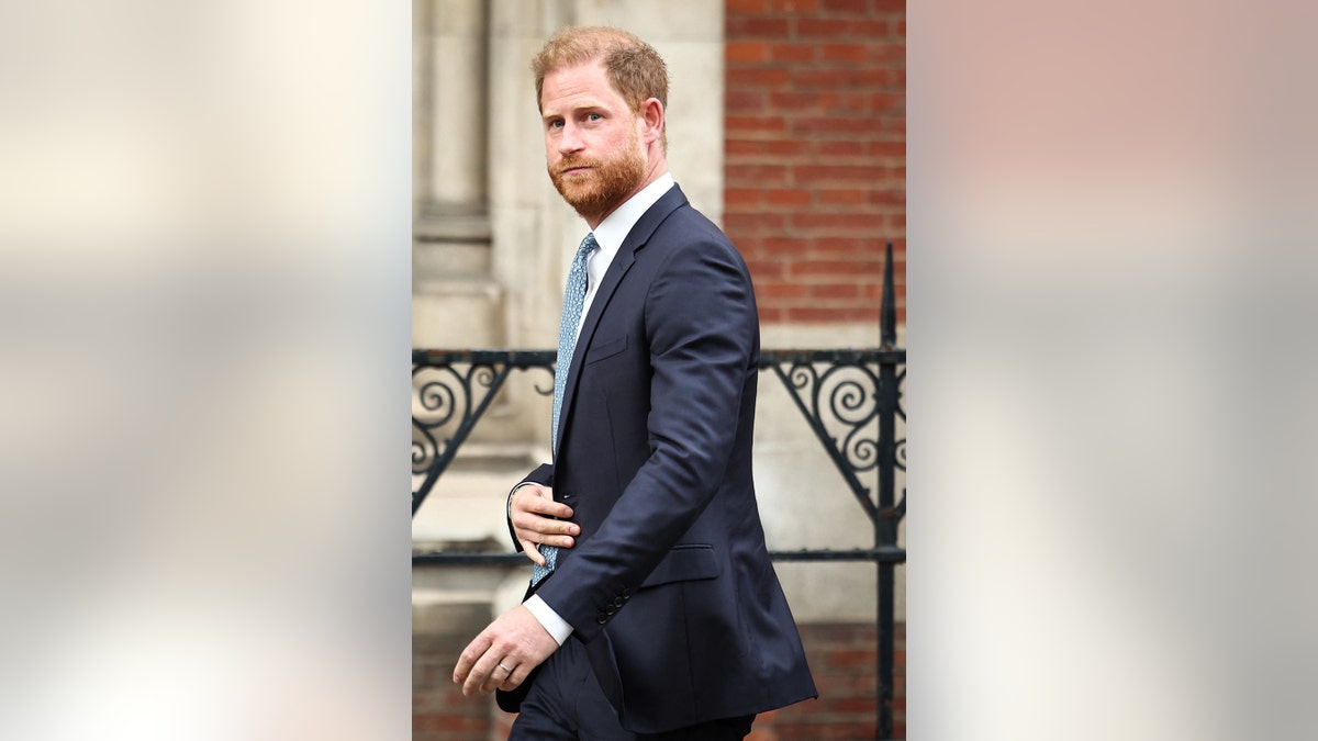 Prince Harry is walking out of his coat wearing a blue suit.