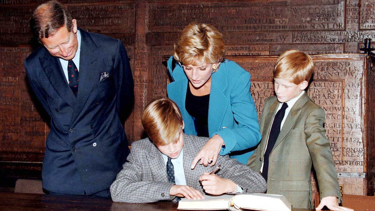 Princess Diana pointed at Prince William sign a book as Prince Charles and Prince Harry look on.