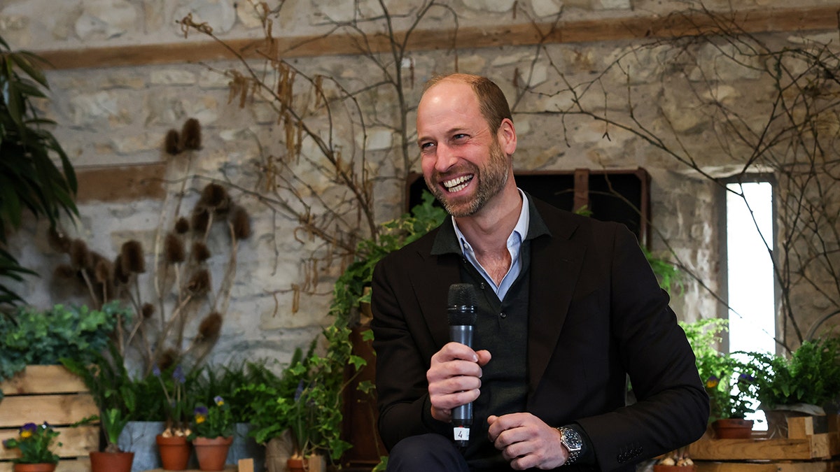 Prince William smiling and holding a mic.