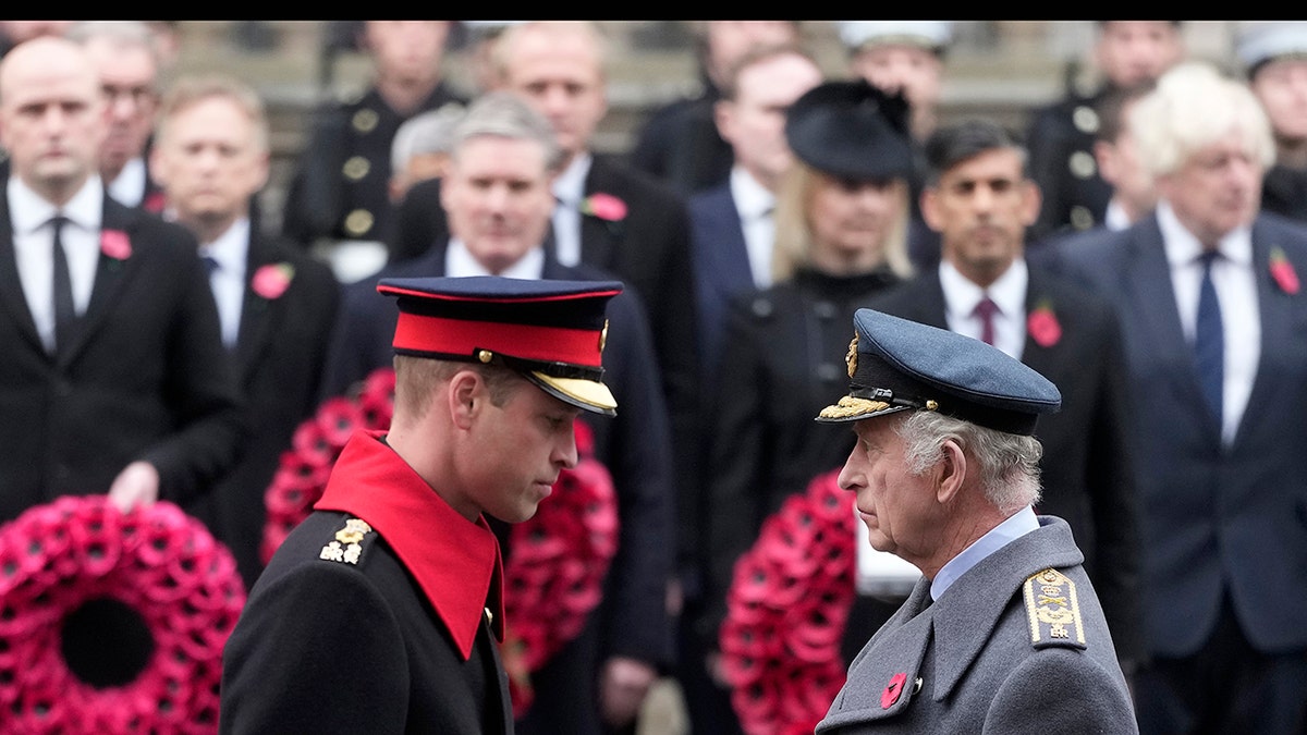 Prince William and King Charles in uniform facing each other outdoors.