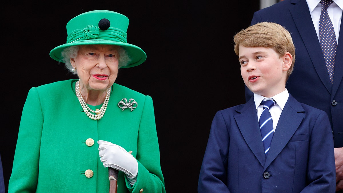 Prince George in a blue suit speaking to his great-grandmother, Queen Elizabeth, in a green suit with a matching hat.