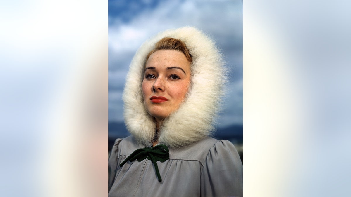 Vera Miles posing in a fur coat with a black ribbon tied in a bow.