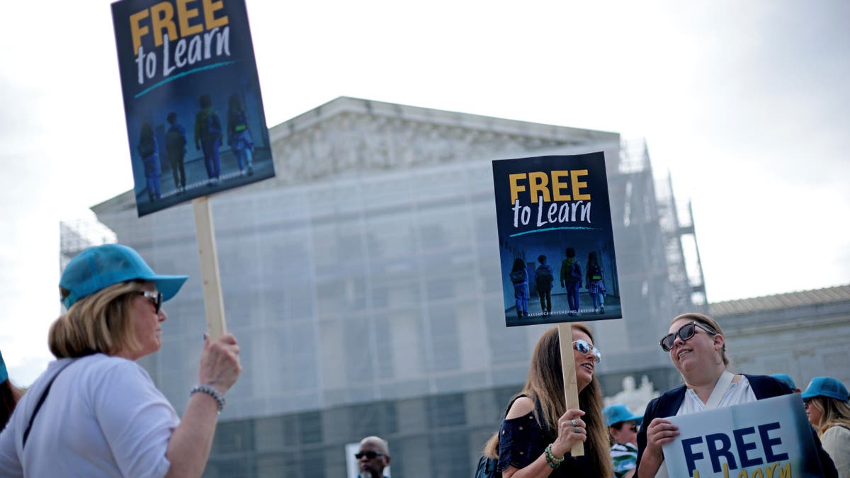Supporters of St. Isidore hold signs outside the Supreme Court.