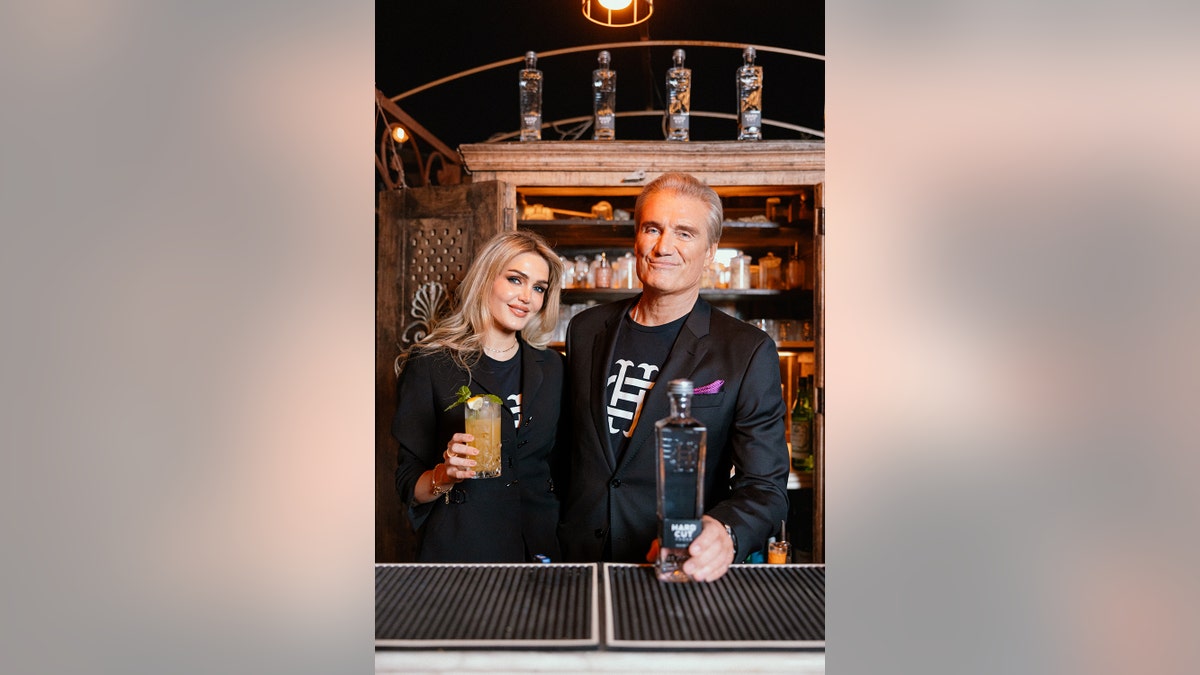 Dolph Lundgren with his wife smiling as they both hold cocktails.
