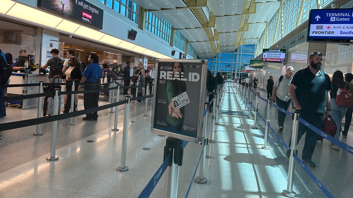 REAL ID sign in a wideshot of an airport full of people.