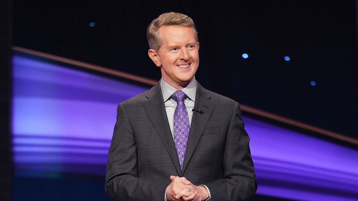 Ken Jennings smiles and stands at a stage at risk