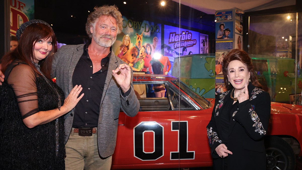 John Schneider being embraced by his wife in front of the General Lee at the Hollywood Museum.