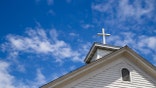 A wooden cross crowns the roof of a traditional white church