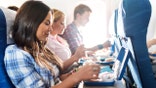 Two women and a man are eating lunch on a plane.