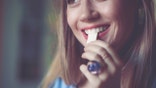 A woman's teeth touch a stick of gum as she smiles.