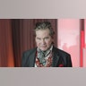 Actor Val Kilmer wears grey blazer and pink shirt.