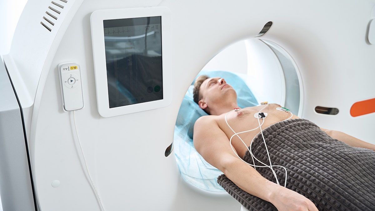 Adult male person with ECG electrodes placed on chest lying in supine position inside CT gantry aperture