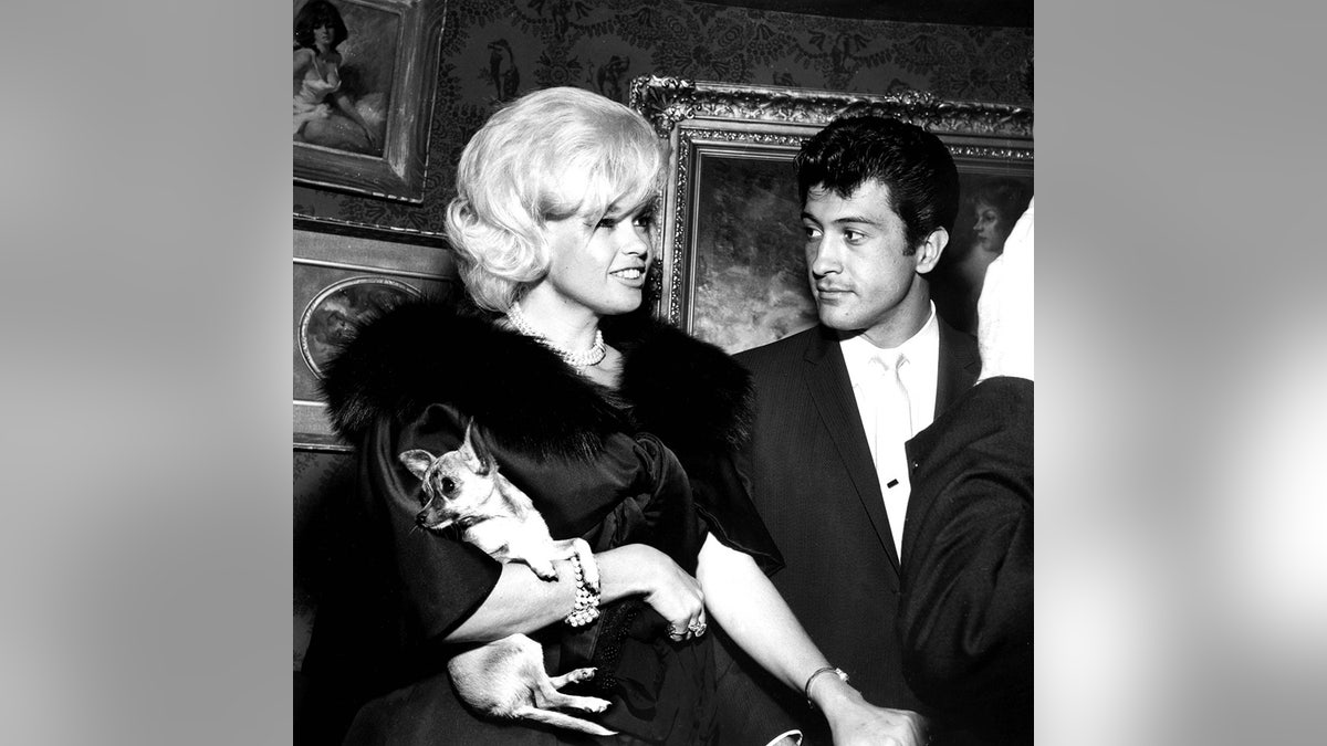 Jayne Mansfield holding her dog next to Nelson Sardelli looking at her.