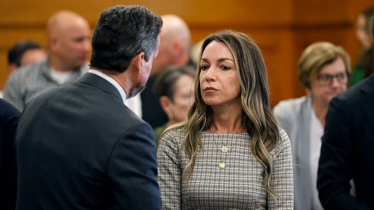 Karen Read, wearing a brown plaid dress, talks with her attorney Alan Jackson, who has his back turned and is wearing a dark suit