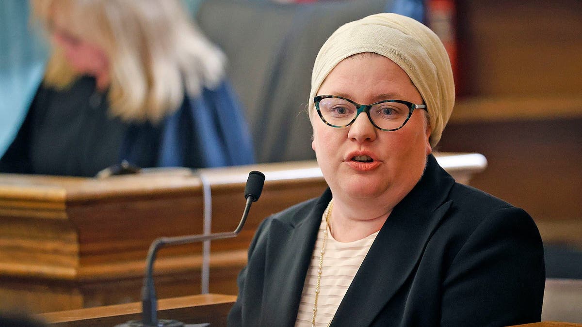 Jessica Hyde on the witness stand wearing a head scarf, black blazer and gold necklace