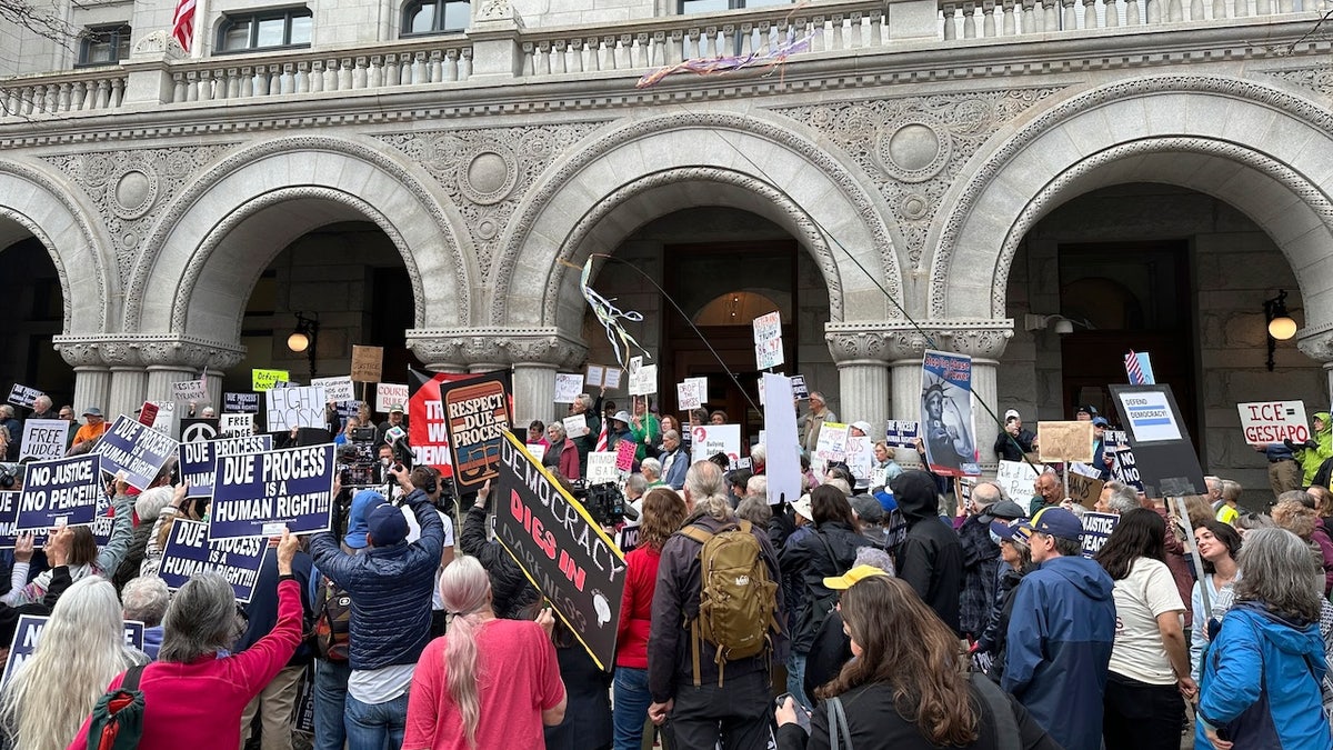 A large crowd of protesters gathers outside a stone federal courthouse with arched entrances, holding signs supporting due process and denouncing ICE. Some signs read