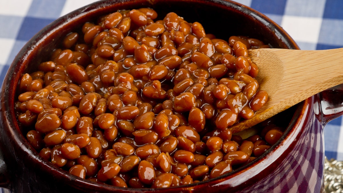 A stirring spoon rests inside a pot of baked beans.