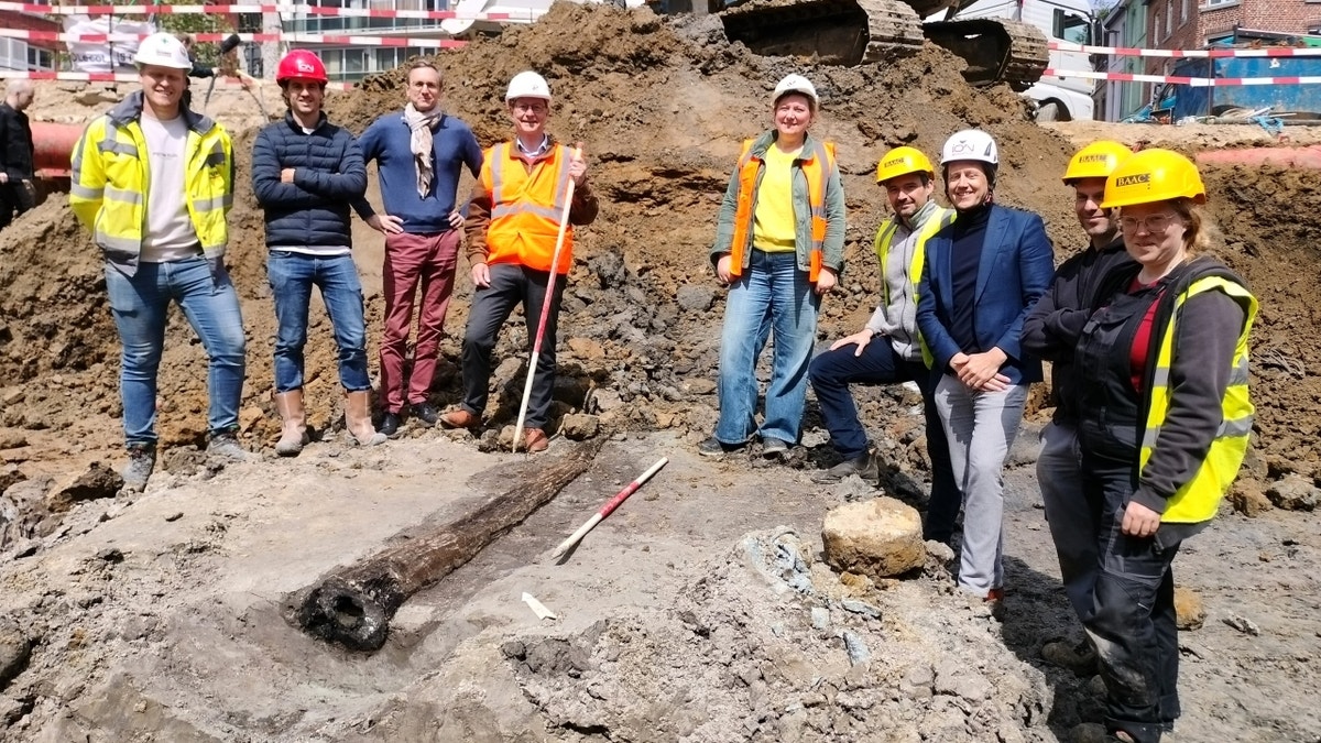 Archaeologists smiling near wooden pipe discovery