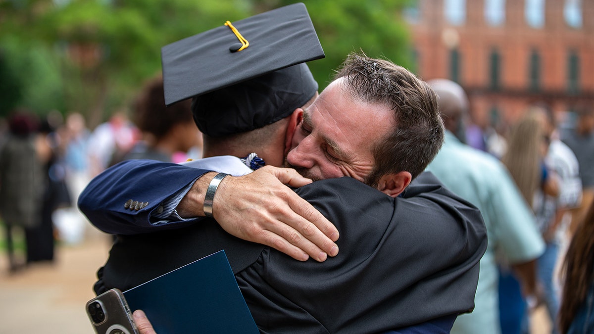 An Chick-Fil-A operator hugs one of the members of his team with a graduation limit and a gown.