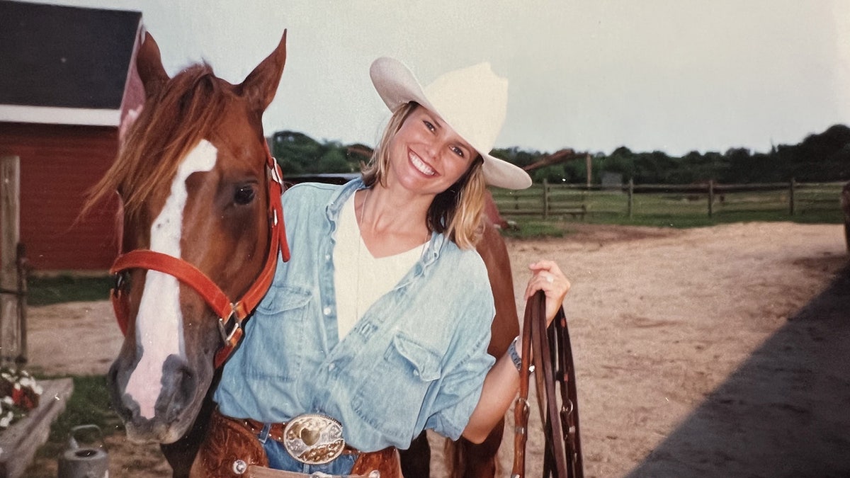Christie Brinkley smiling in cowboy gear next to a horse.
