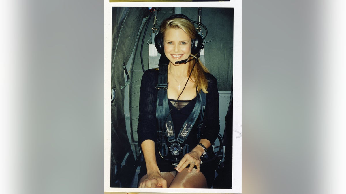 A close-up of Christie Brinkley smiling wearing headphones inside a plane.