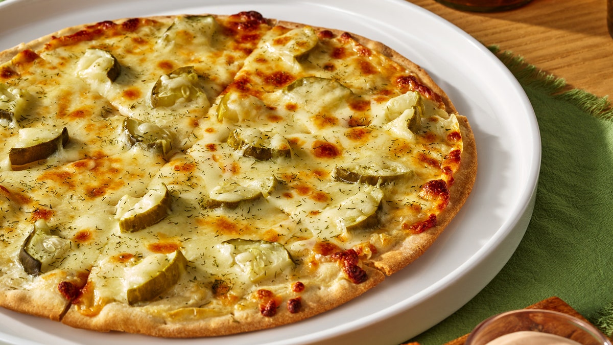 California Pizza Kitchen's frozen dill pickle pizza rests on a white hot plate on top of a green table cloth.