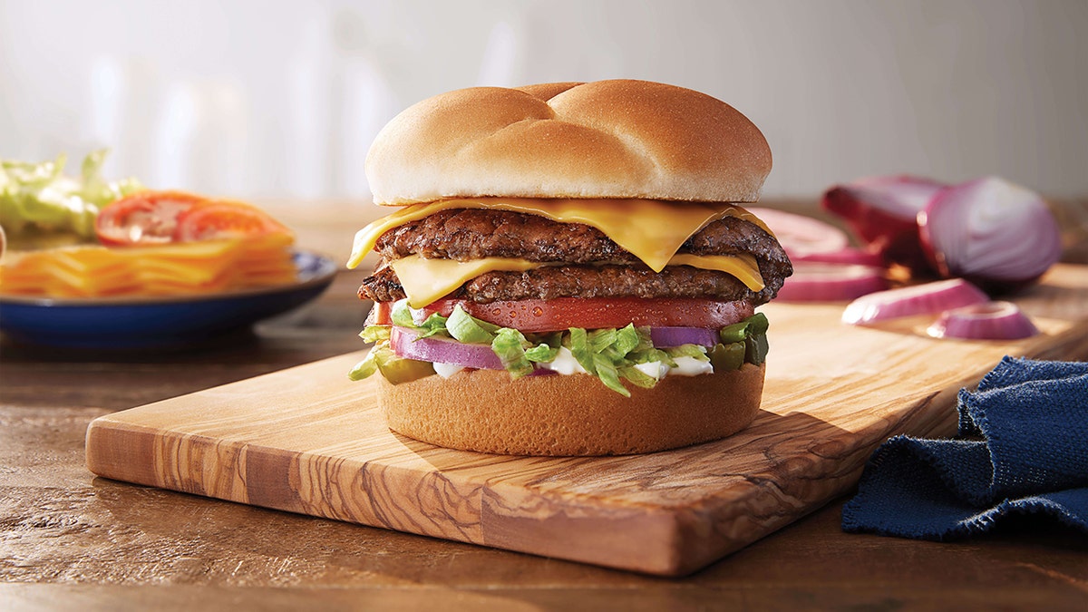 A Culver's Double Deluxe ButterBurger is shown on a wooden table with some ingredients in the background.