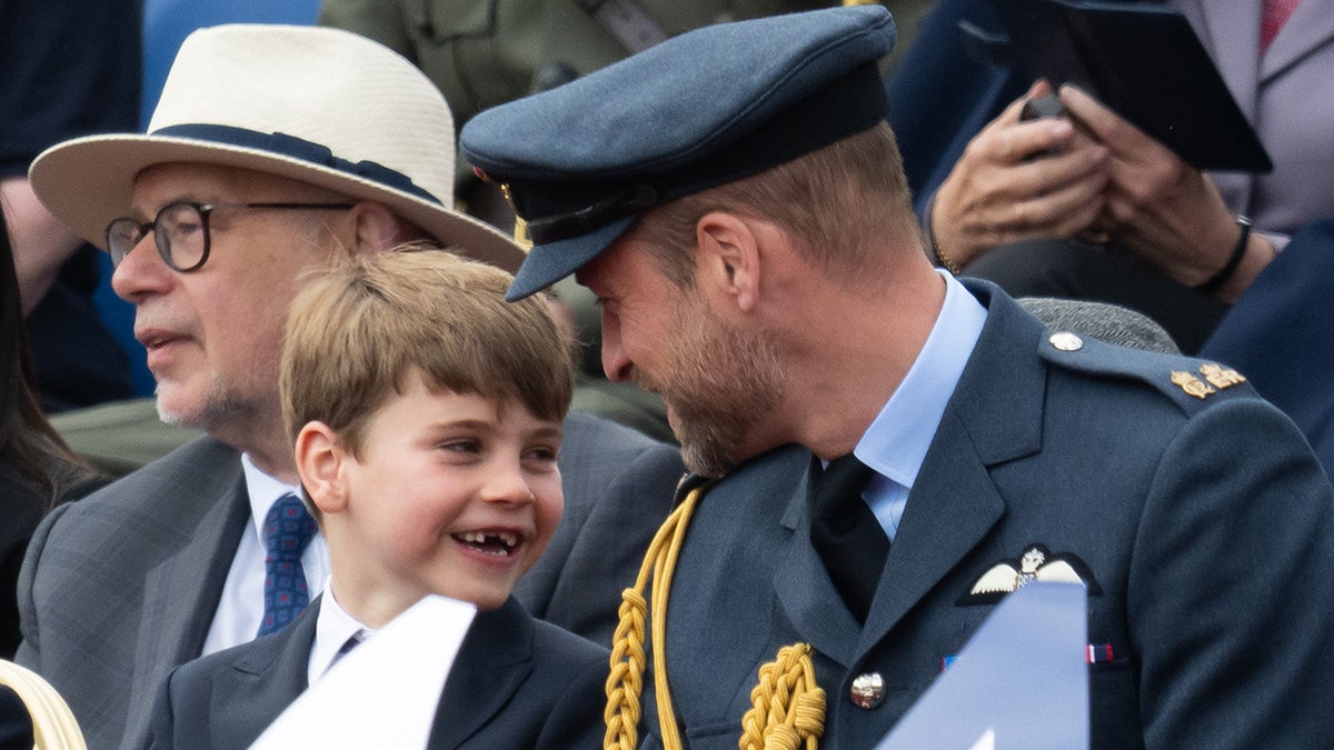 Prince Louis giving a smiling Prince William in uniform a toothless grin.