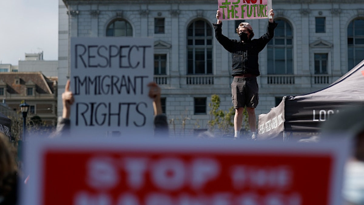 Protesters hold up signs during a demonstration in front of a large government building. One sign reads