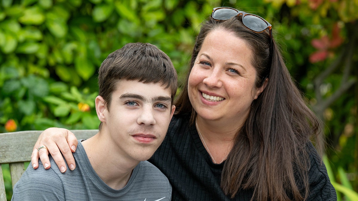 Finley Ranson and his mother pose for a photograph on a bench outside.