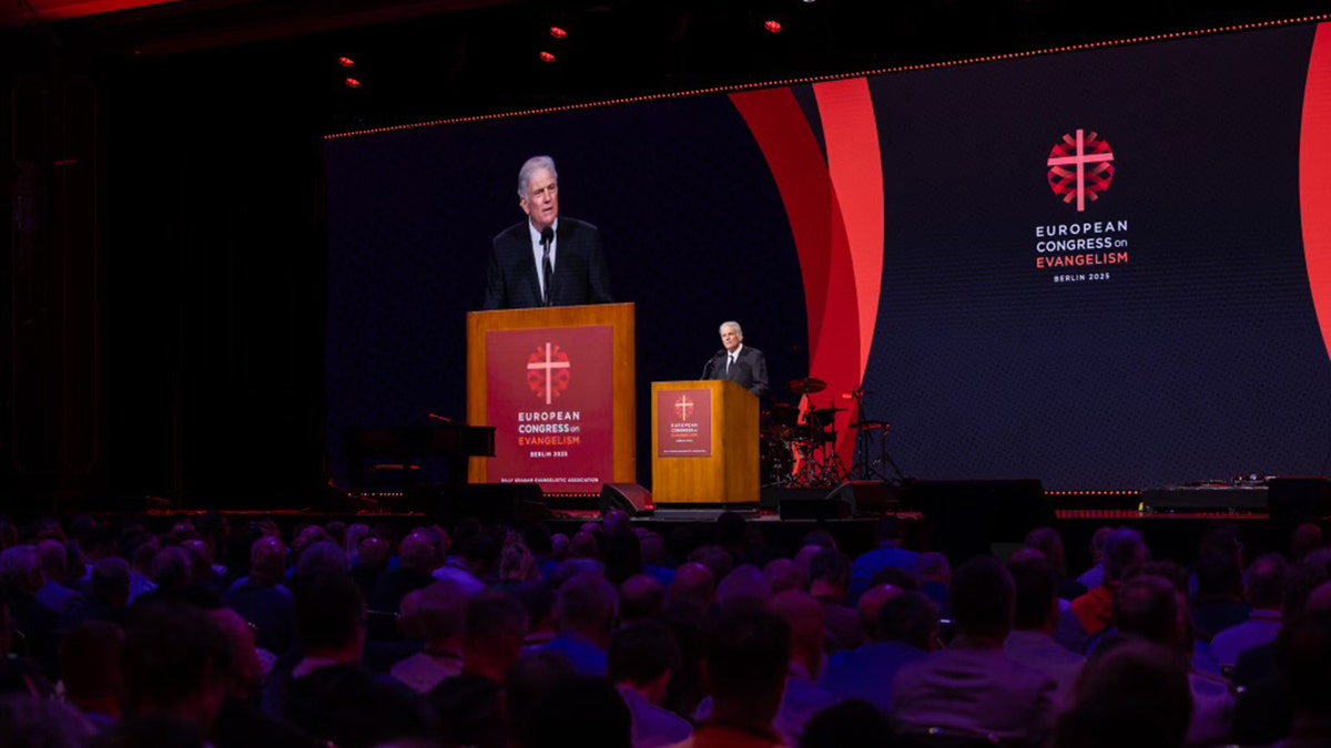 Franklin Graham speaks at the podium during the European Congress on Evangelism in Berlin, with his image projected on a large screen behind him
