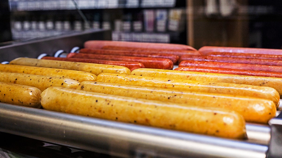 Hot dogs and sausages rotate under a warmer at a gas station.