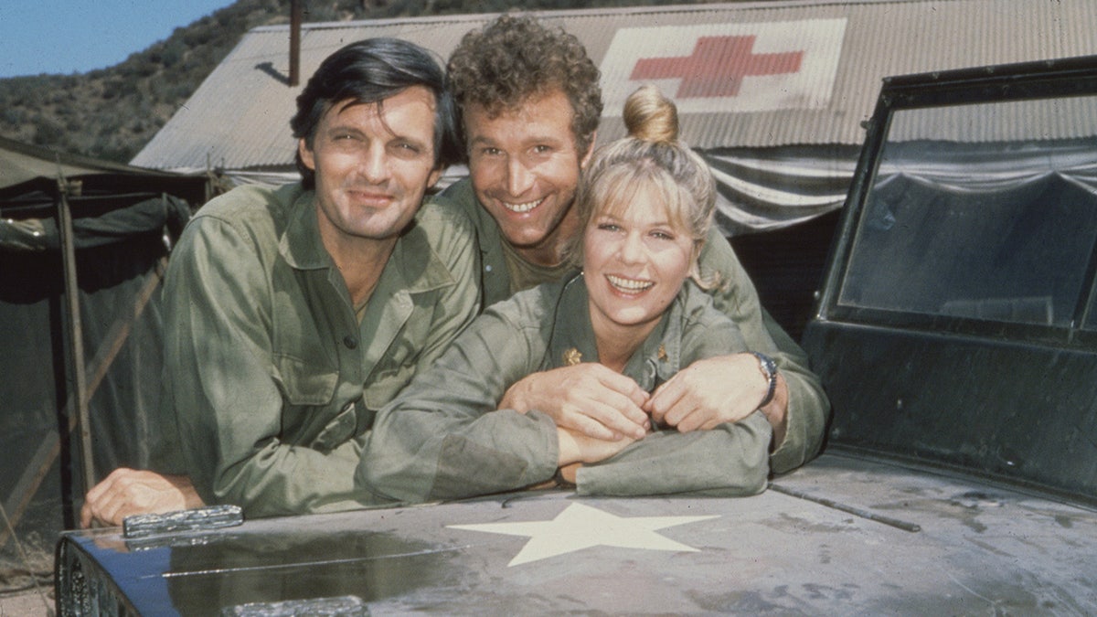 The cast of "M*A*S*H" in costume embracing each other.