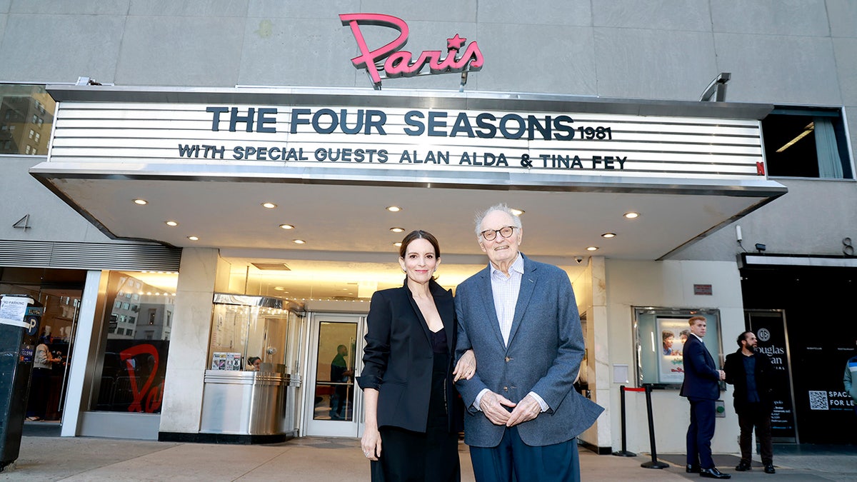 Alan Alda in a blue blazer and white shirt standing next to Tina Fey outside The Paris Theater.