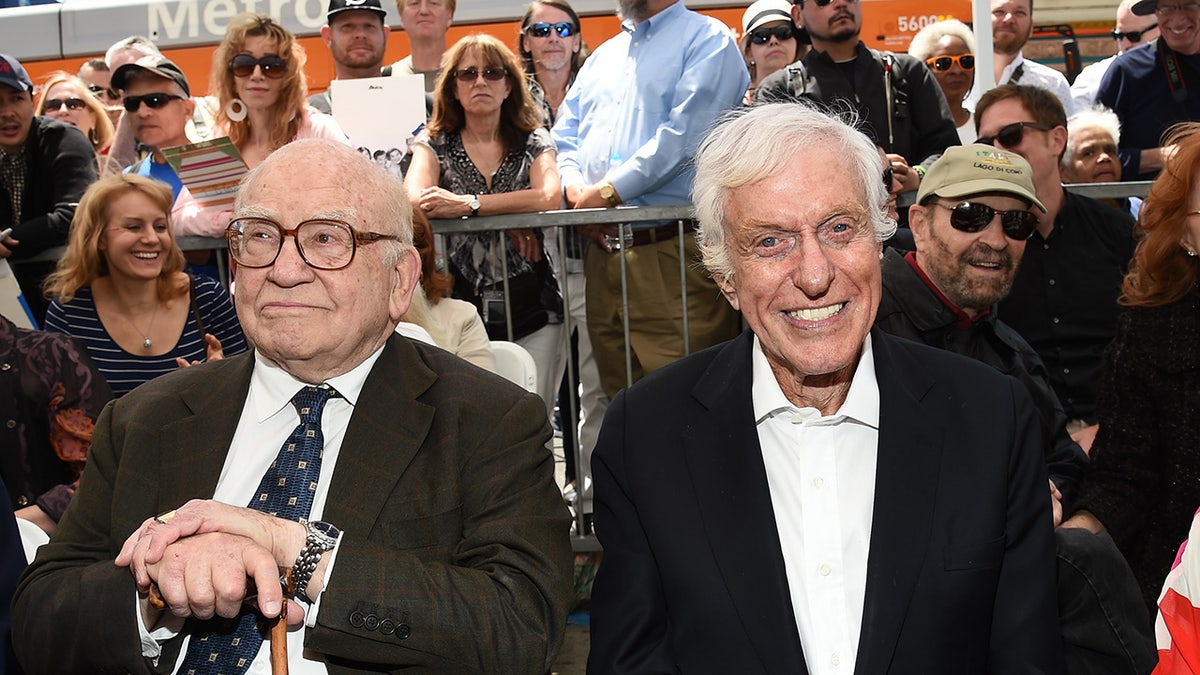 Ed Asner holding a cane sitting next to a smiling Dick Van Dyke.