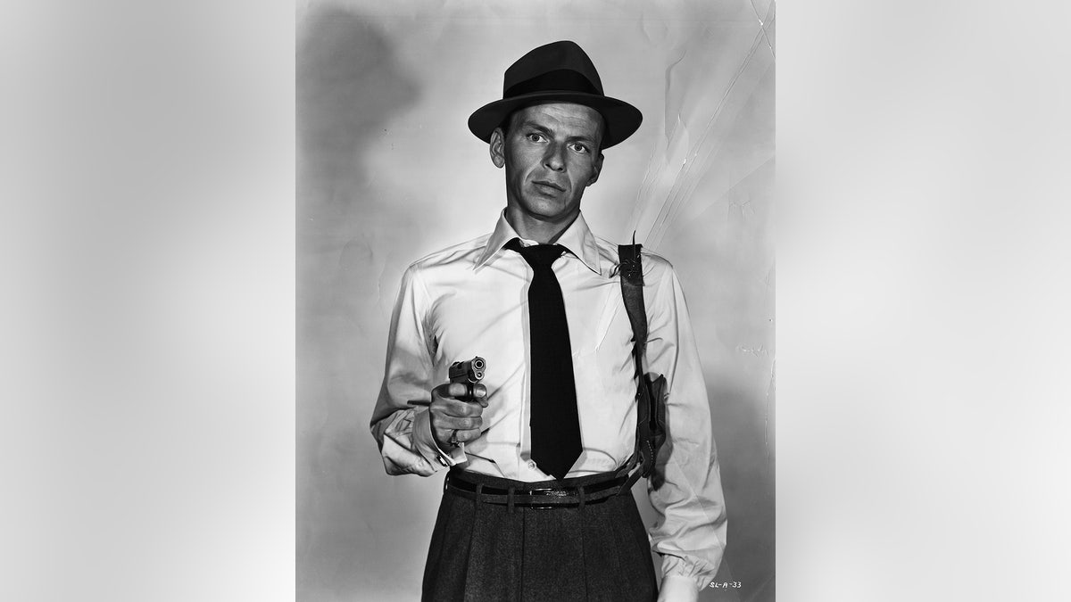 Frank Sinatra wearing a shirt and tie holding a gun.