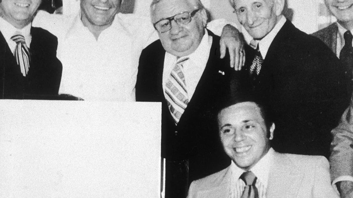 Frank Sinatra smiling and embracing a group of reputed mobsters.