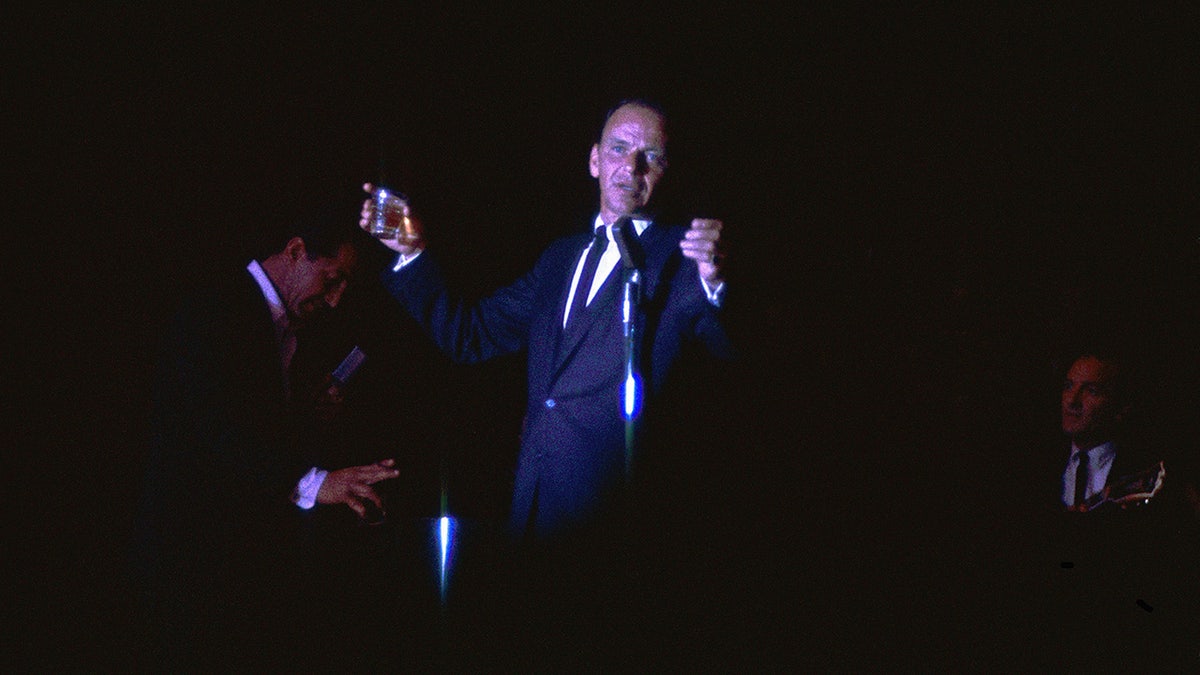 Frank Sinatra performing on stage holding a glass of Jack Daniels