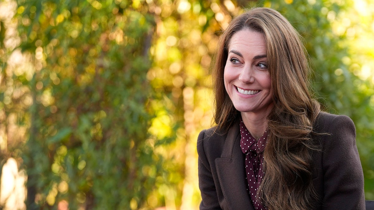 Kate Middleton smiling and wearing a brown blazer with a burgundy polka dot blouse.
